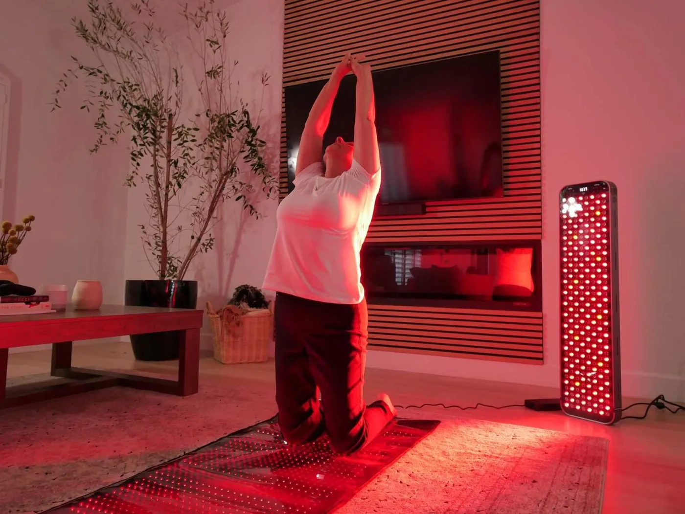 At home: a woman stretching on an ORA red light mat in her living room, next to a standing ORA panel