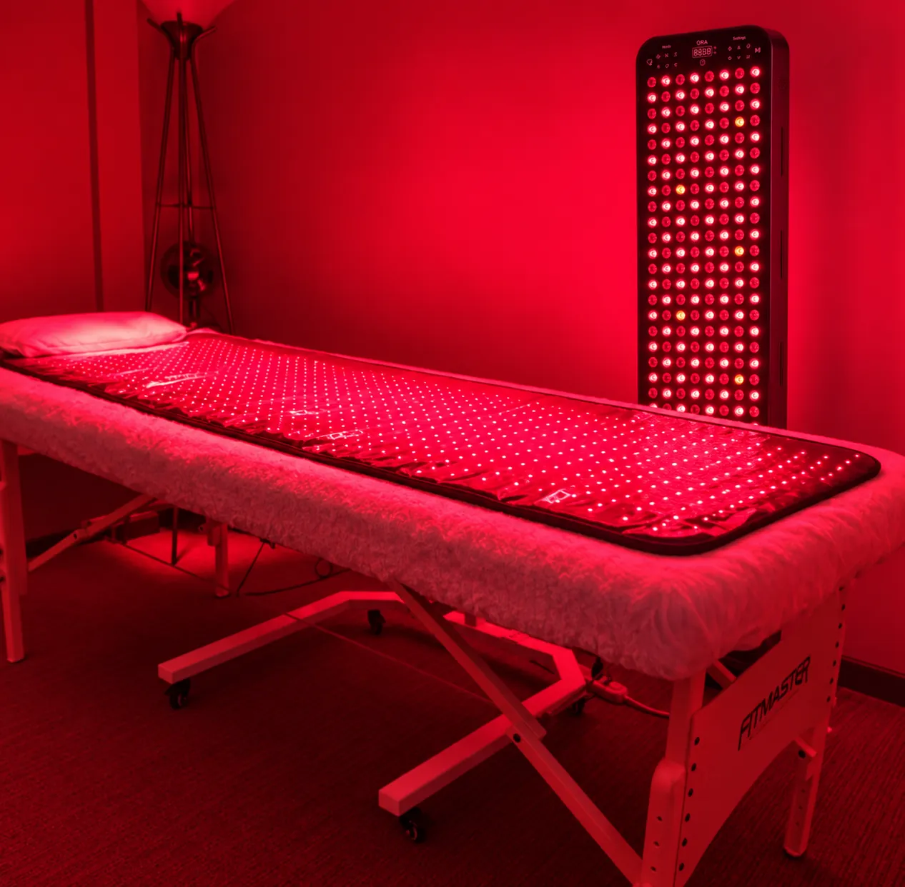 Treatment room with a full-length red LED mat on a massage bed and a tall red light panel standing beside it